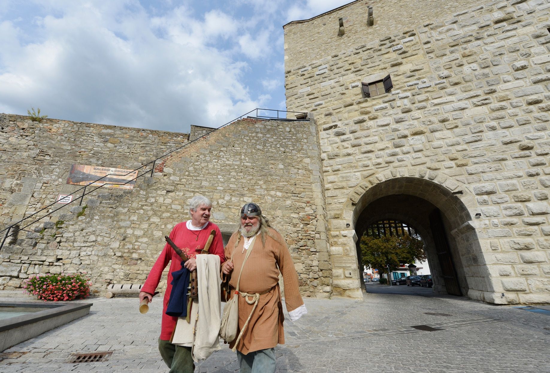 Dvaja muži v stredovekom oblečení pred starým kamenným múrom v Hainburgu an der Donau.