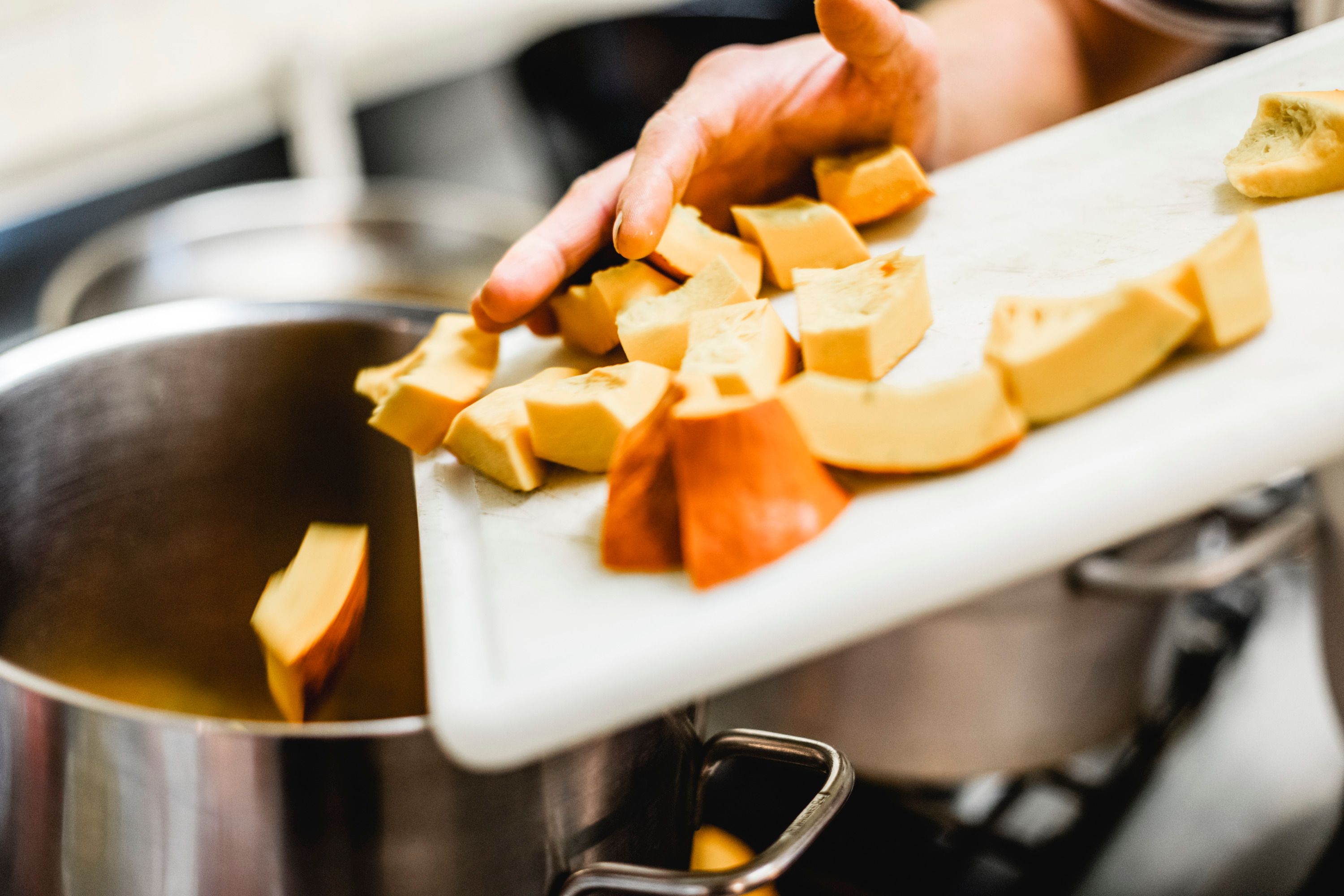 Ruka tlačí nakrájané kúsky tekvice z dosky na krájanie do hrnca.