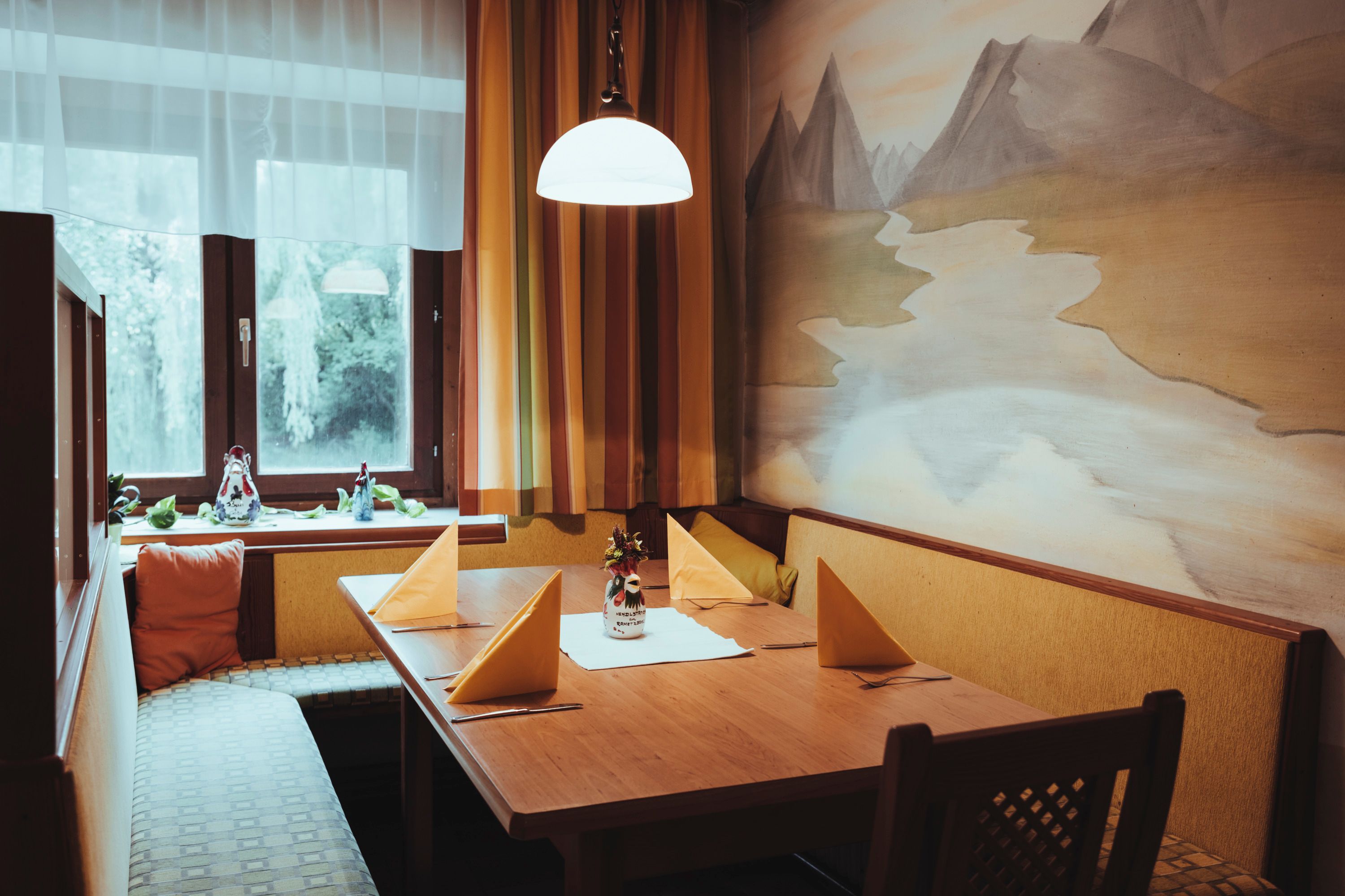 Útulné posedenie s dreveným stolom, žltými obrúskami a maľbou na stene v reštaurácii.