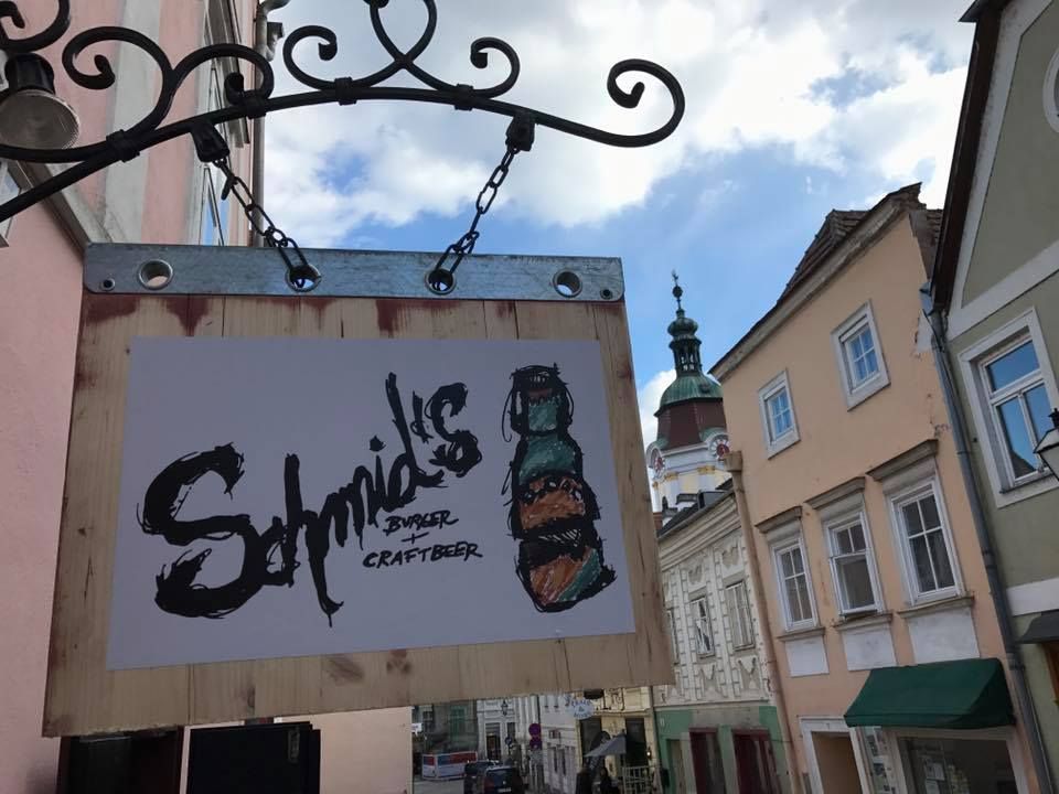Nápis Schmid's Burger and Craftbeer na stene domu v starej mestskej ulici.