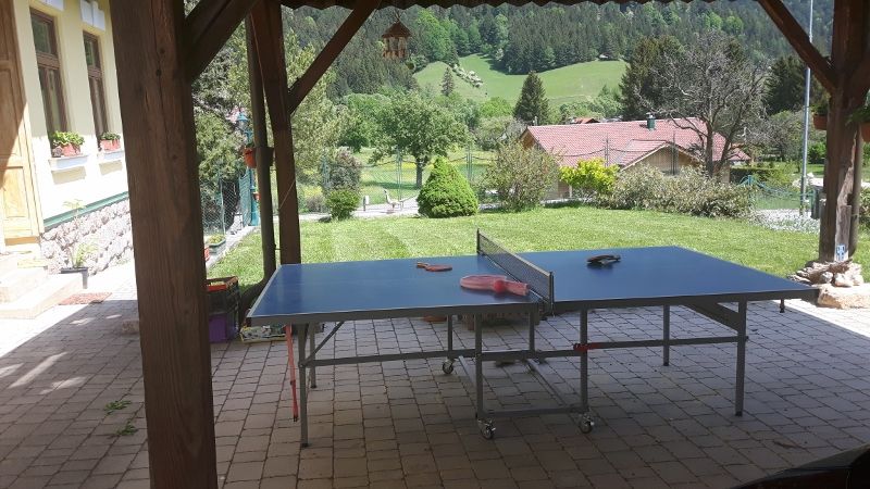 Stôl na stolný tenis pod prístreškom s výhľadom na zelenú záhradu a kopce v pozadí.