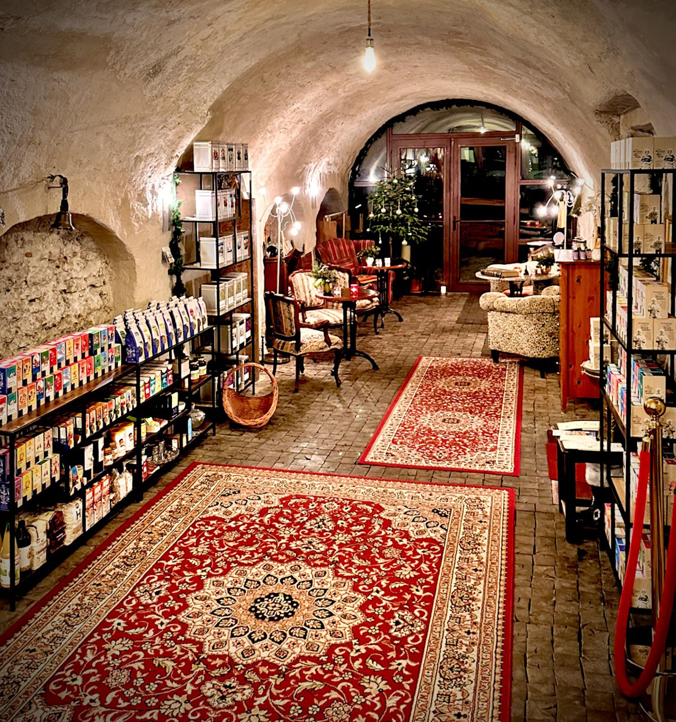 Útulná miestnosť s červenými kobercami, policami plnými výrobkov a posedením v čajovni.