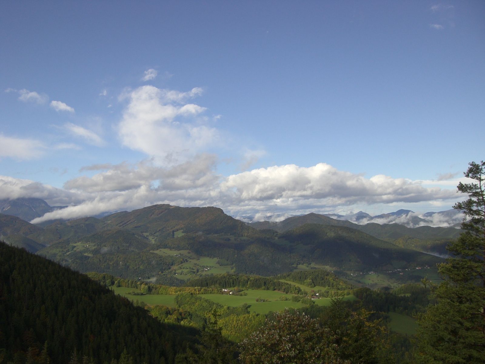 Panoramatický pohľad na zelenú horskú krajinu pod modrou oblohou s mrakmi.