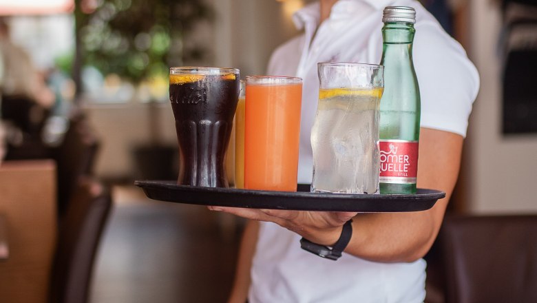 Usmievav&aacute; ča&scaron;n&iacute;čka pod&aacute;va n&aacute;poje na podnose v &uacute;tulnej re&scaron;taur&aacute;cii.