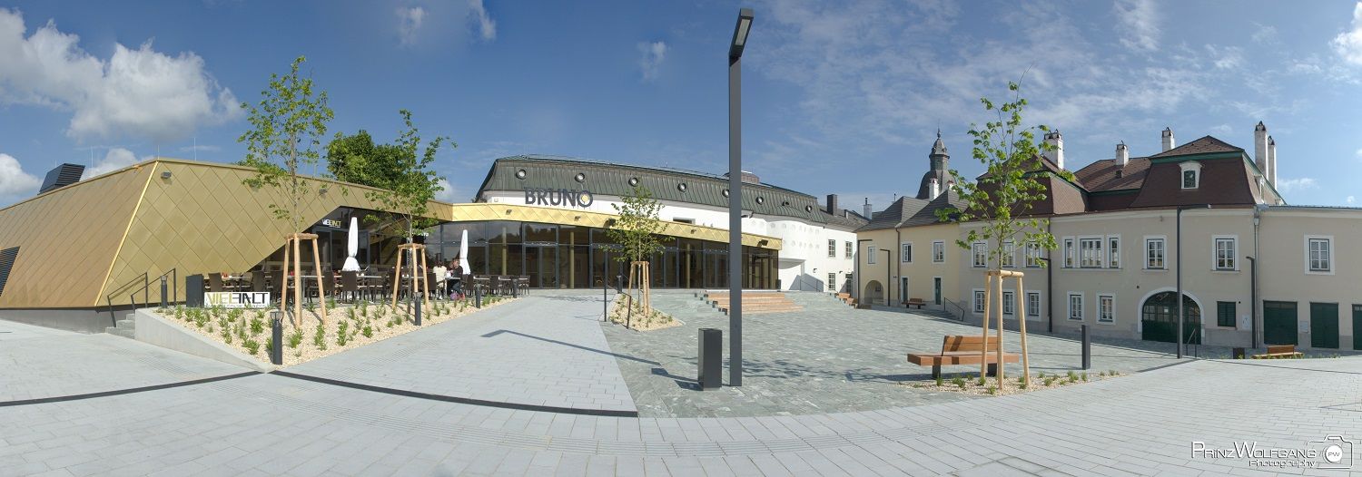 Moderná architektúra so zlatou fasádou a tradičnou budovou v pozadí, modrá obloha.