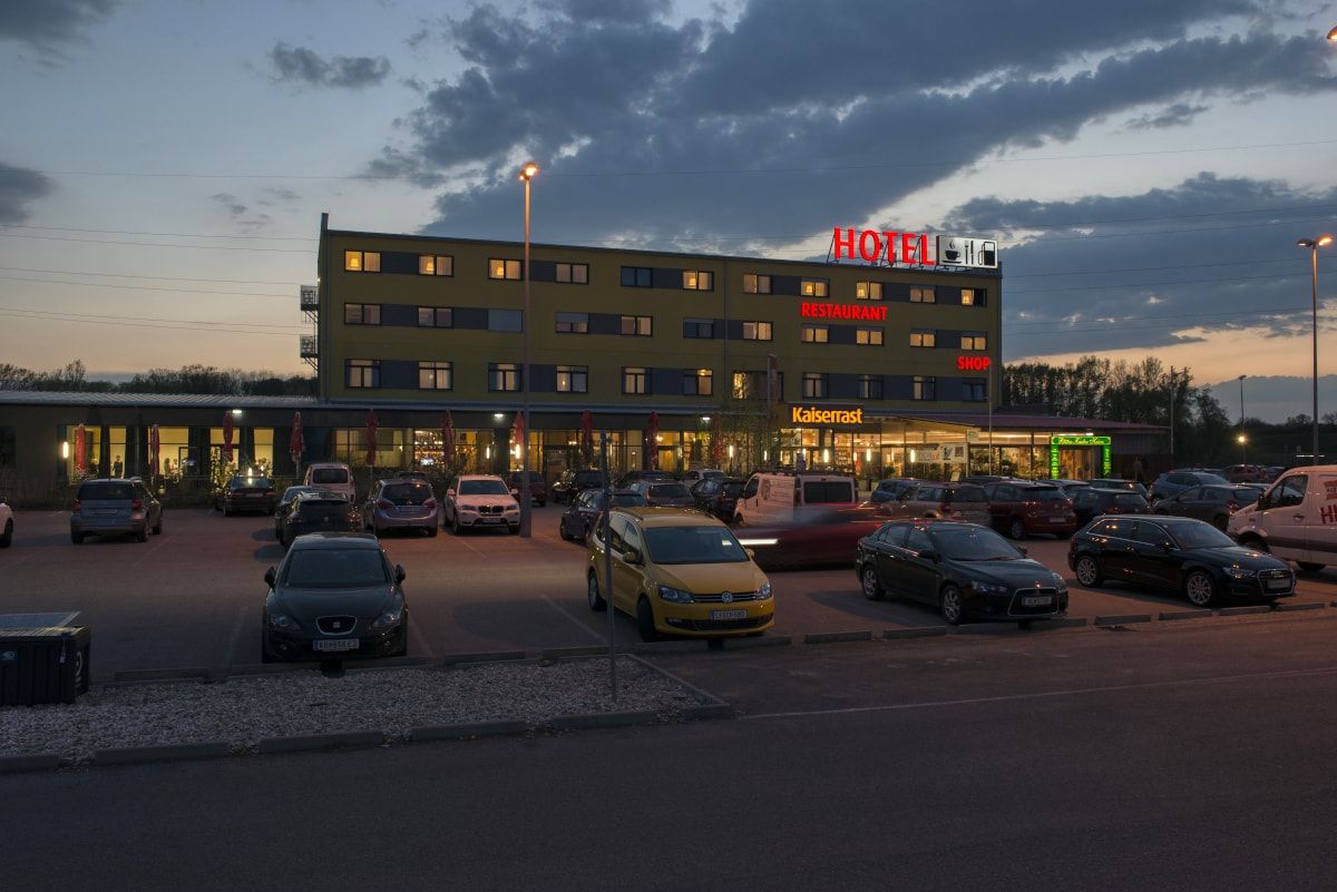 Večerný záber na hotel s parkoviskom a autami pred ním.