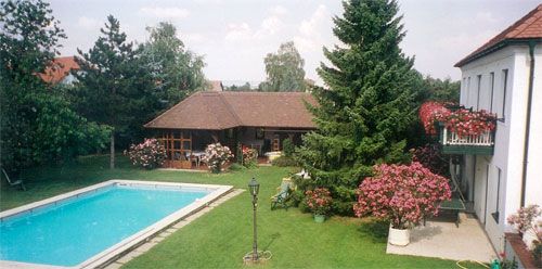 Udržiavaná záhrada s bazénom, stromami a domom s balkónom.