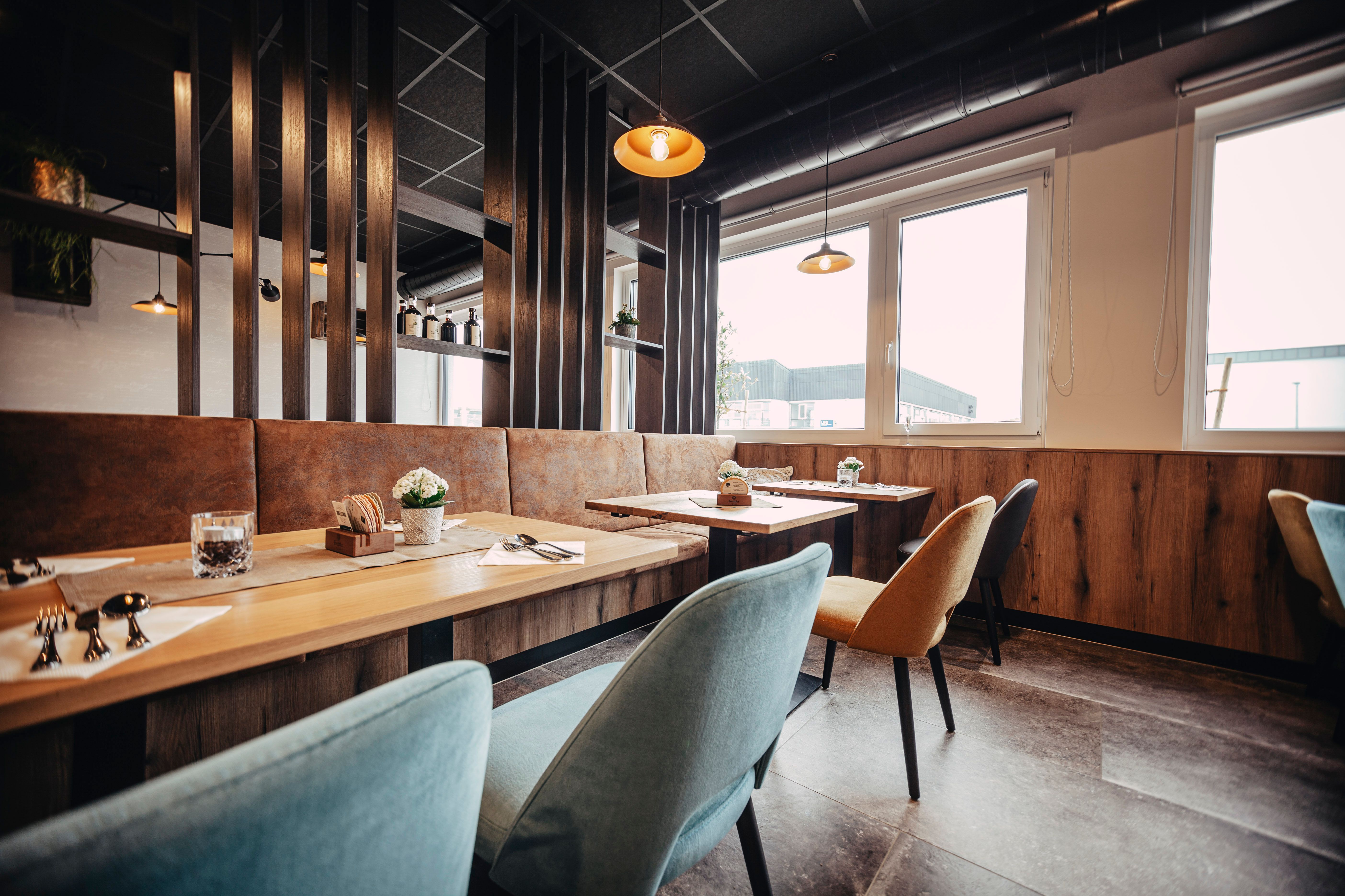 Moderná reštaurácia s drevenými stolmi, farebnými stoličkami a veľkými oknami.