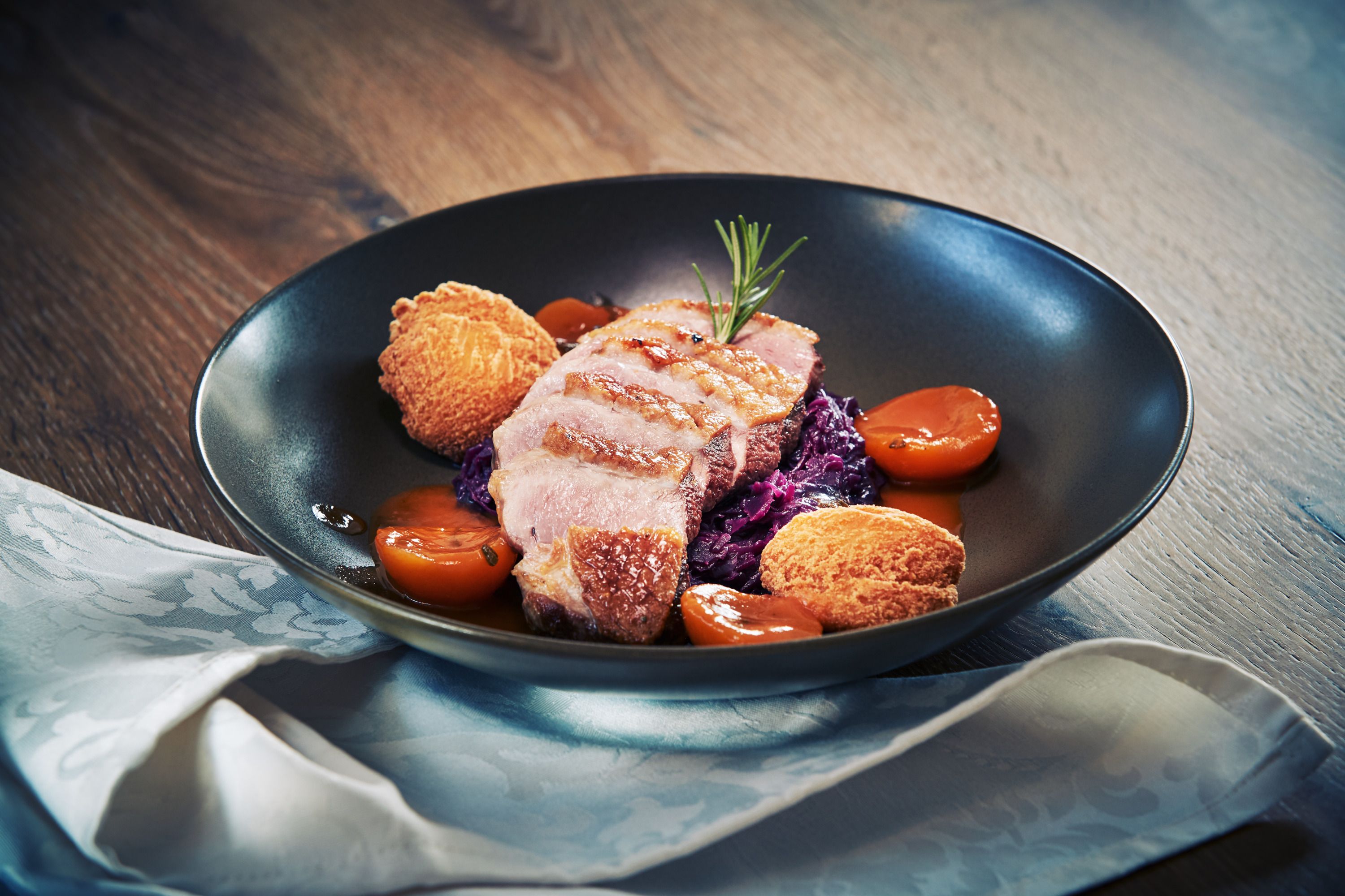 Gurmánske jedlo s kačacími prsiami, červenou kapustou, zemiakovými knedľami a marhuľami na čiernom tanieri.