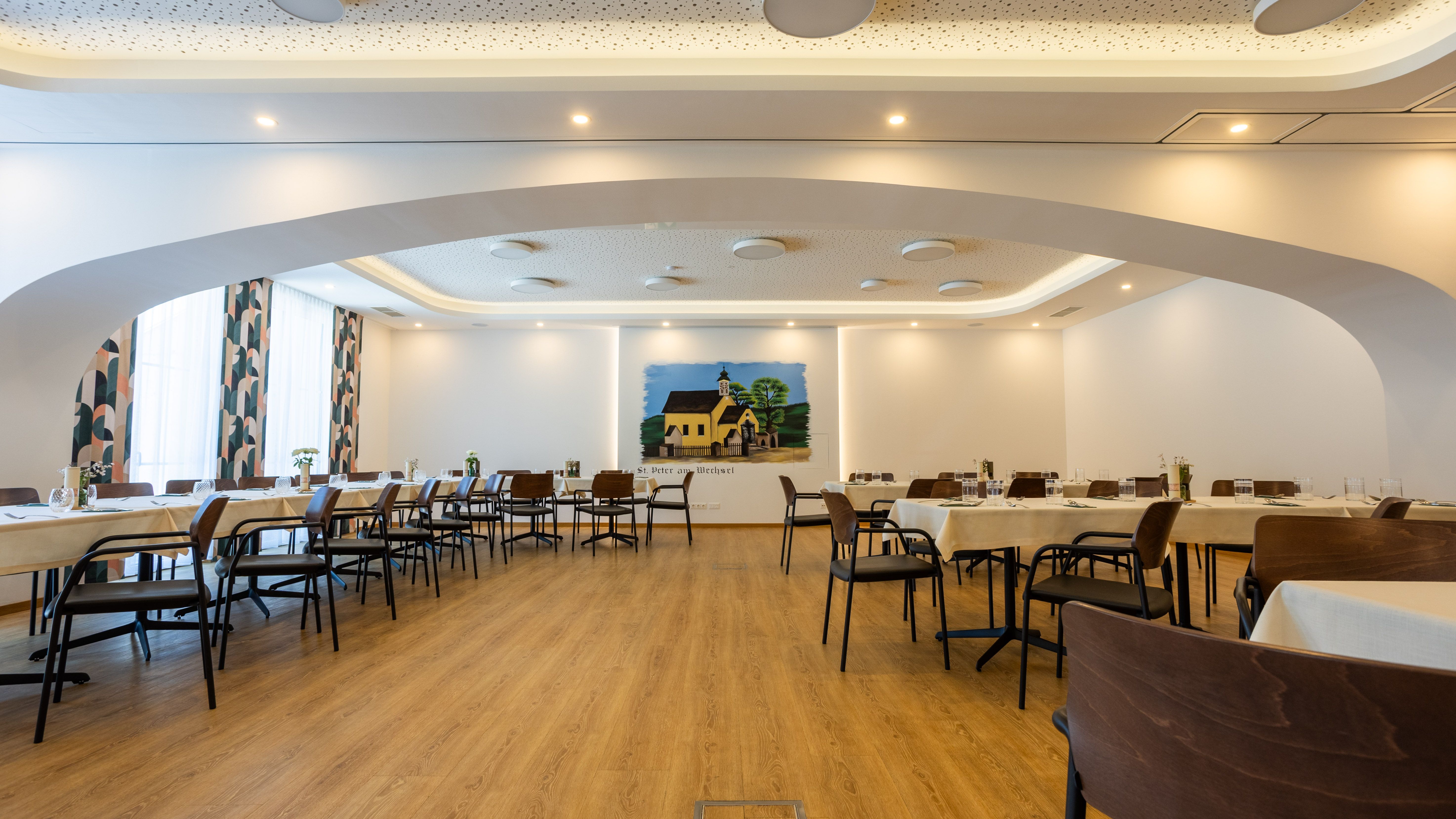 Pohľad do interiéru modernej krčmy s položenými stolmi a nástennou maľbou.