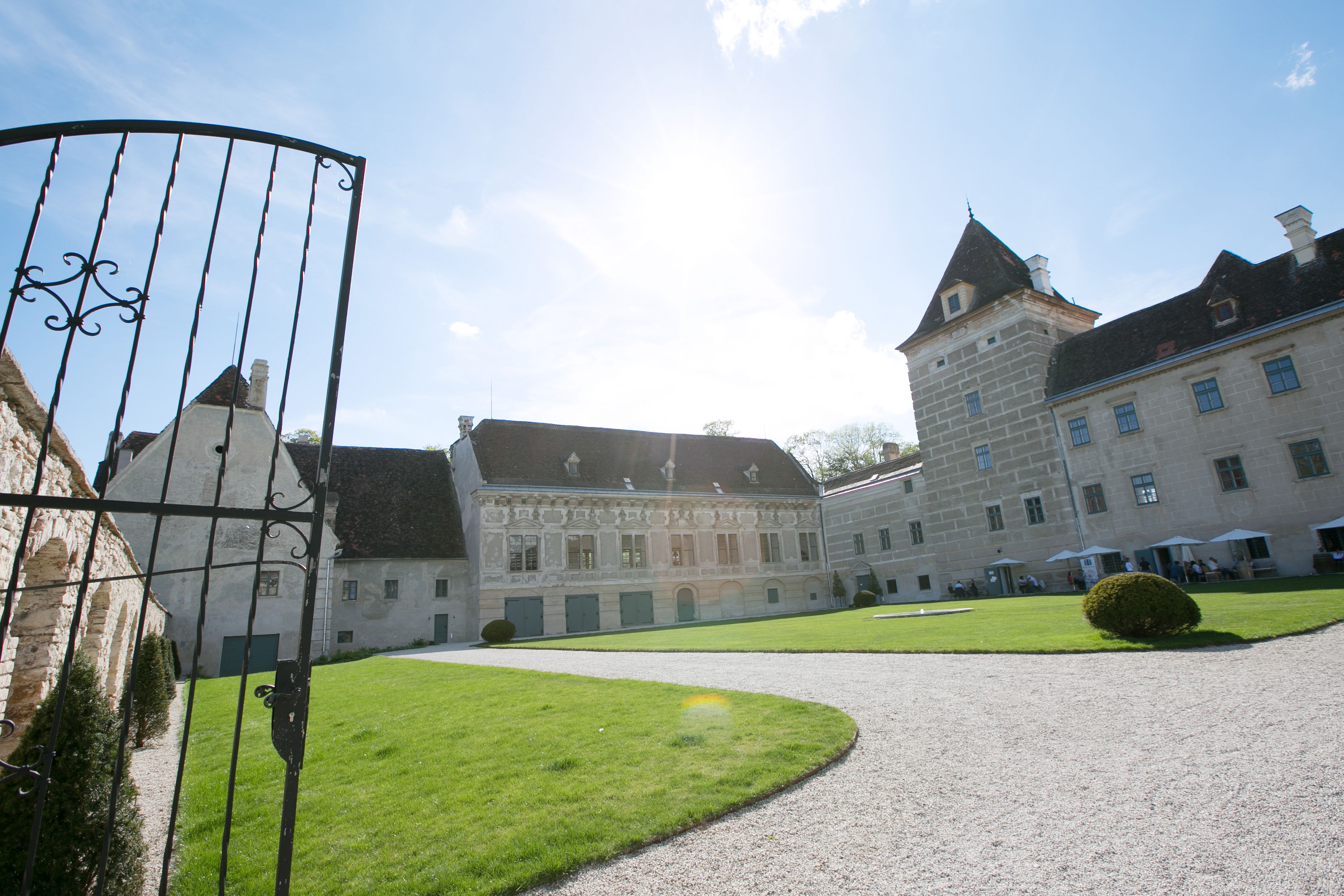 Vstup do zámku Walpersdorf s otvorenou bránou, trávnikom a historickou budovou v pozadí.