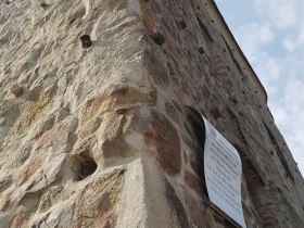 Z&aacute;ber zbl&iacute;zka na star&uacute; kamenn&uacute; vežu s informačnou tabuľou na stene.