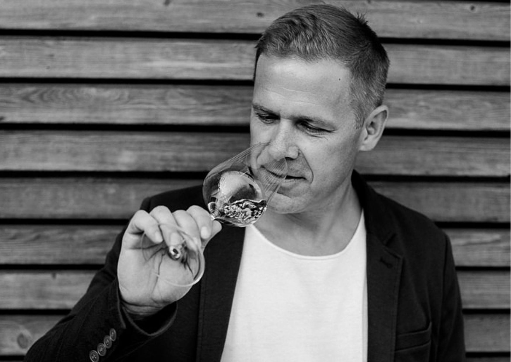 Muž čuchá pohár vína pred drevenou stenou.