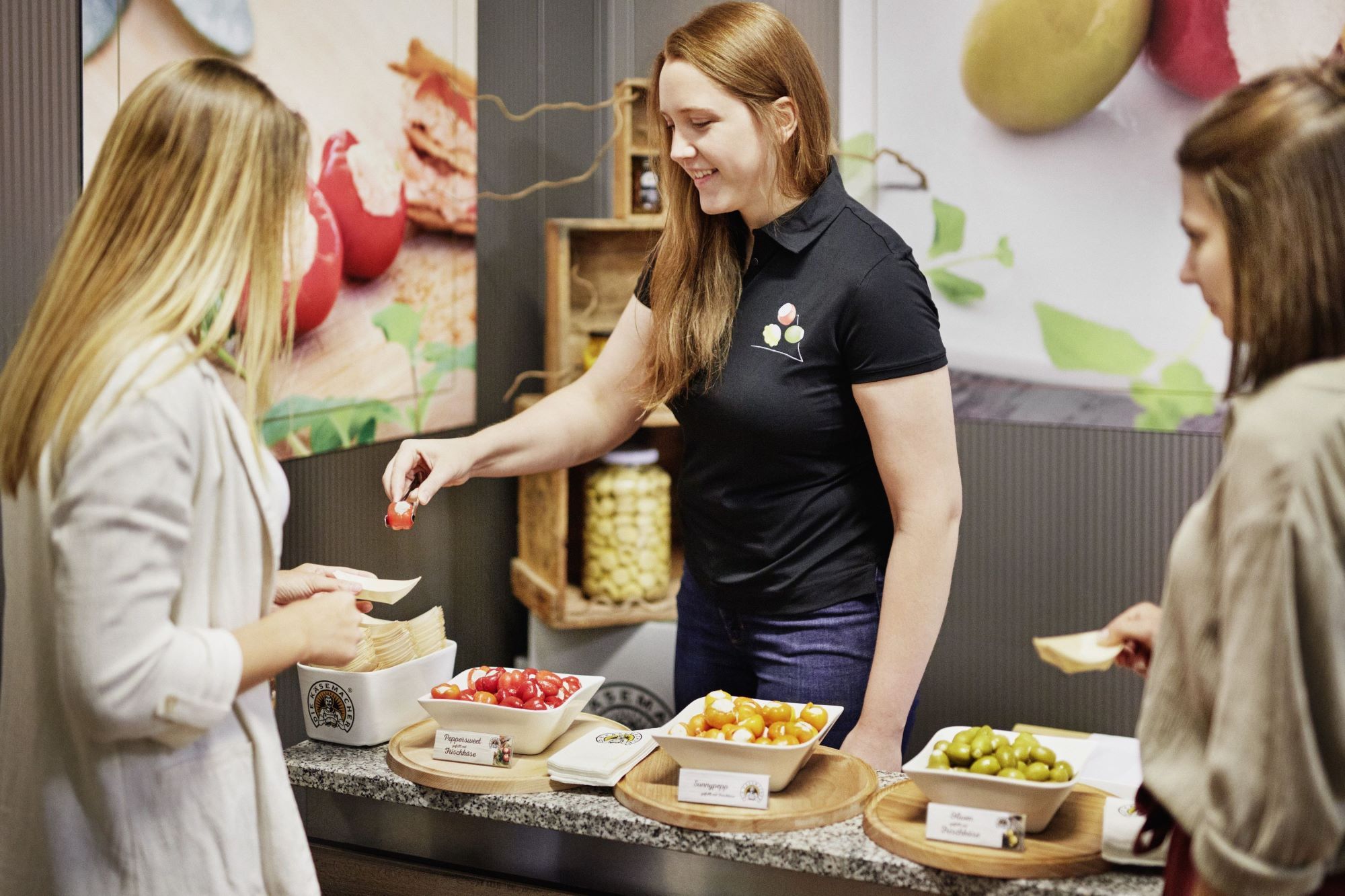 Žena ponúka dvom ďalším ženám na ochutnanie rôzne plnené papriky a olivy.