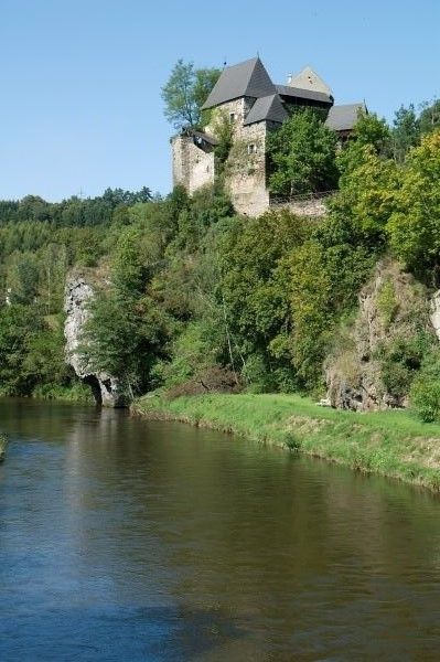 Hrad na zalesnenom kopci na brehu rieky.