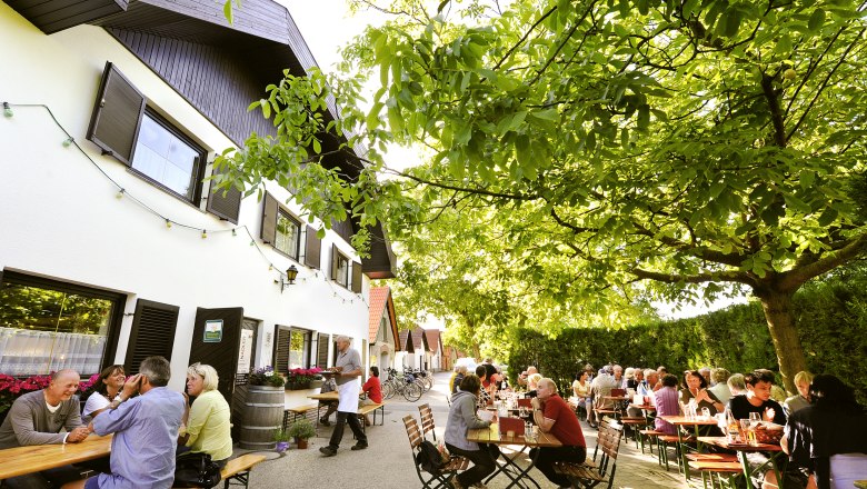 Ľudia sediaci pri vonkaj&scaron;&iacute;ch stoloch pod stromami vo vin&aacute;rni.