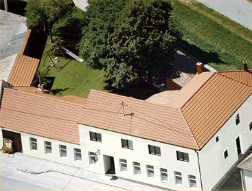 Letecký pohľad na komplex budov s červenou strechou a vnútorným dvorom so stromami a detským ihriskom.