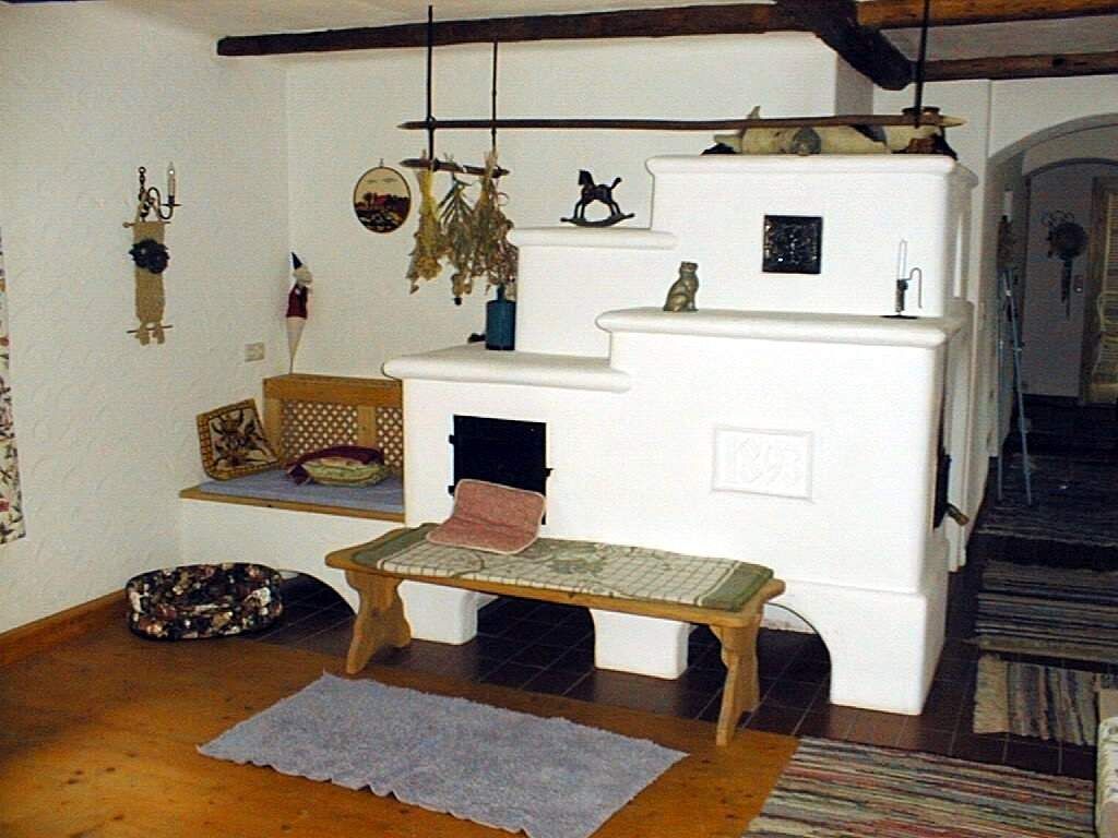 Útulná izba s bielou kachľovou pecou a drevenými trámami.