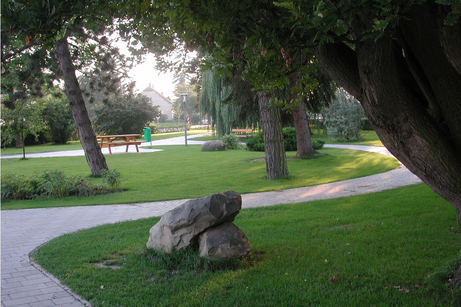 Udržiavaný park so stromami, chodníkmi a lavičkami.
