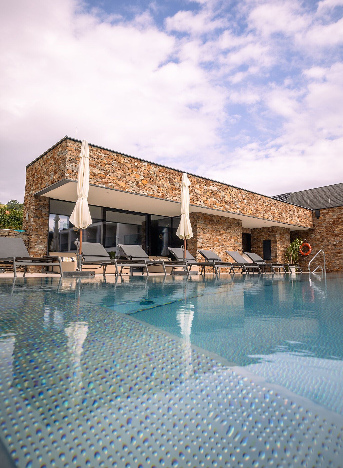 Exteriérový pohľad na moderný hotel s bazénom a ležadlami.