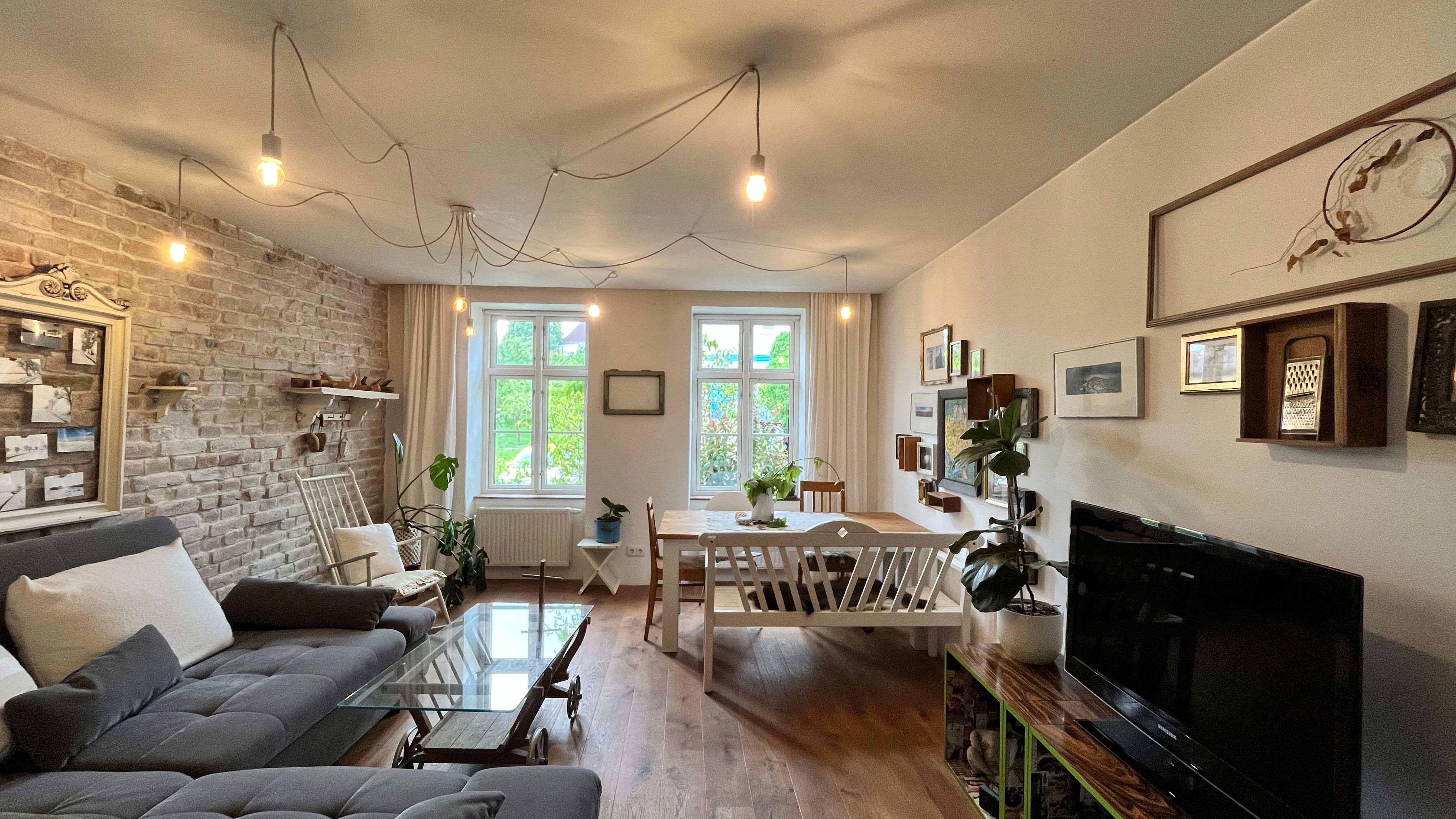 Útulná obývacia izba so sivou pohovkou, dreveným stolom, rastlinami a nástennými dekoráciami.