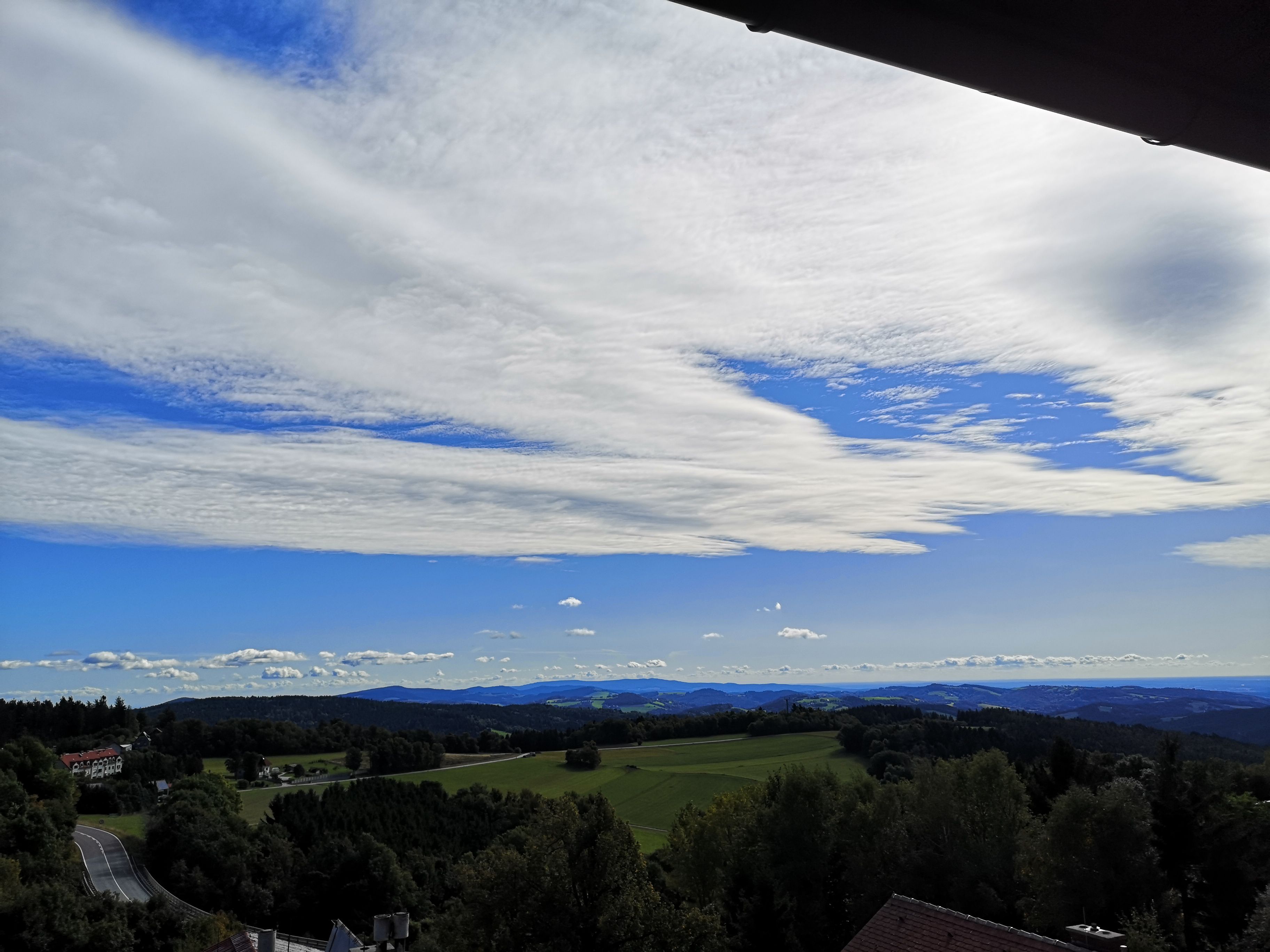 Krajina s kopcami, lesmi a širokou oblohou s mrakmi.
