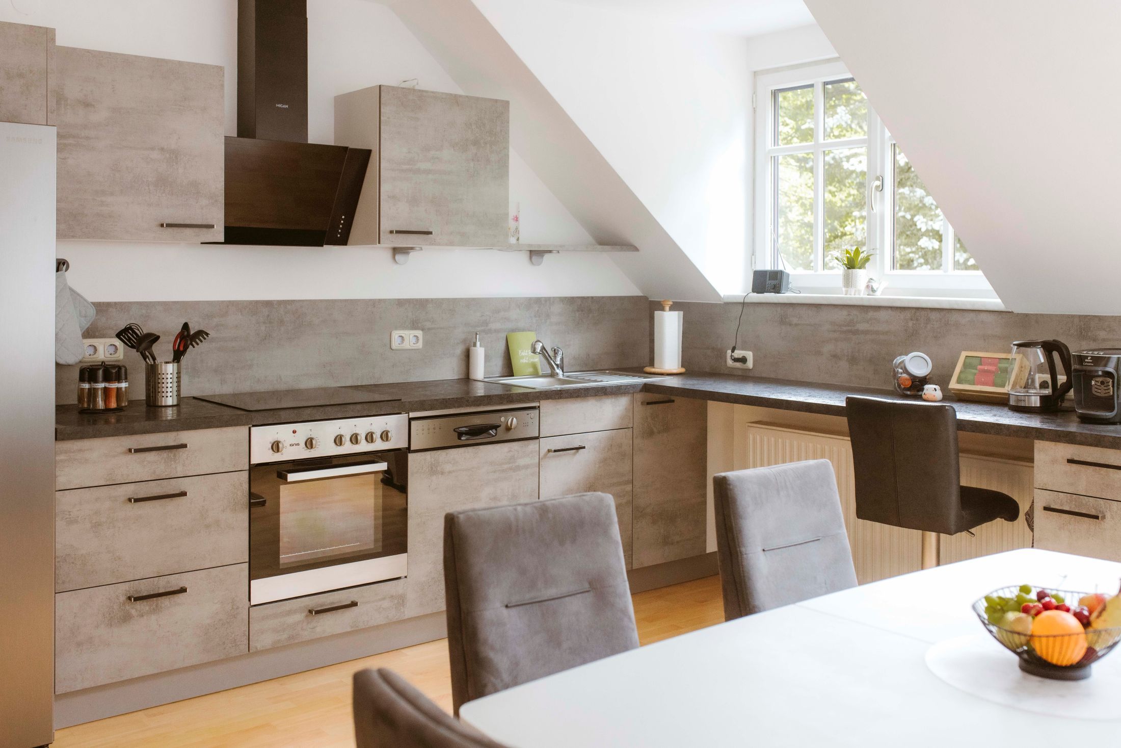 Moderná kuchyňa so sivými skrinkami, jedálenským stolom a miskou na ovocie.