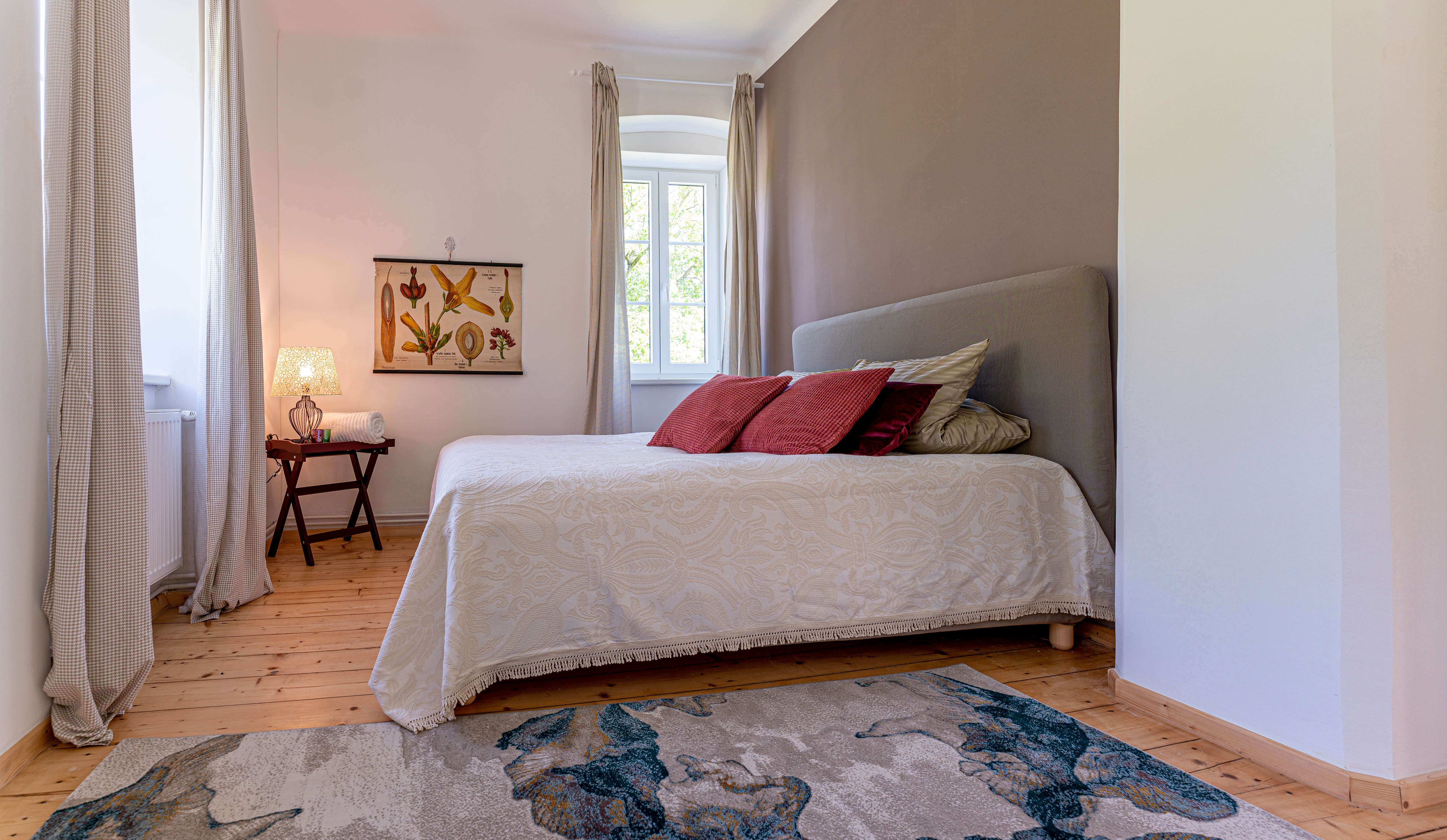 Spálňa s posteľou, červenými vankúšmi, kobercom a oknom so závesmi.