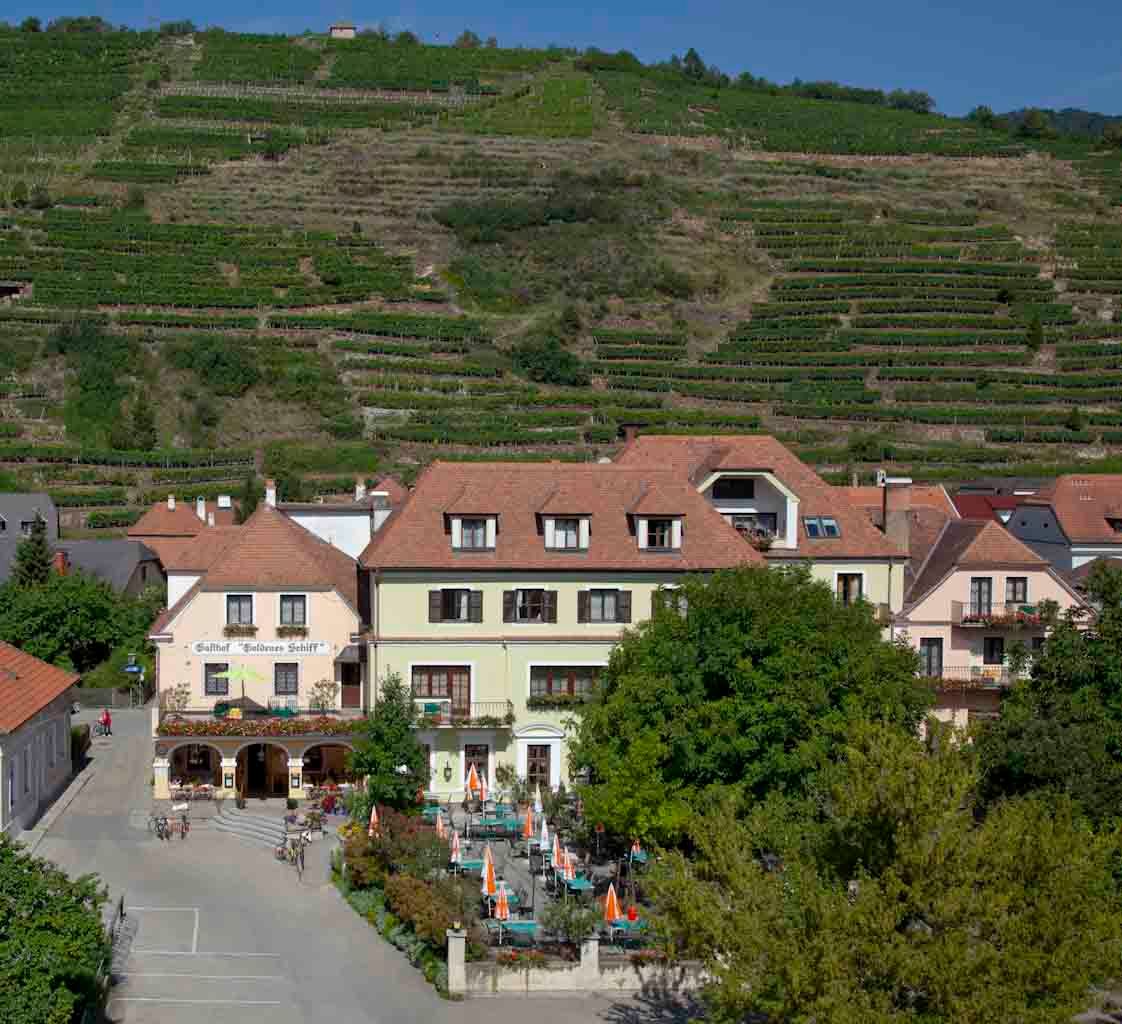 Exteriérový pohľad na hostinec s terasou a vinicami v pozadí.
