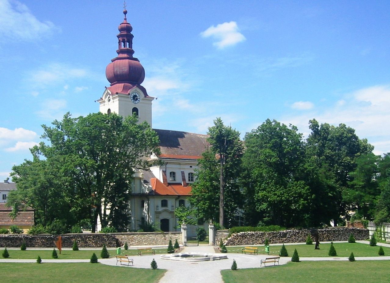 Barokový kostol s červenou vežou a záhradou v popredí.
