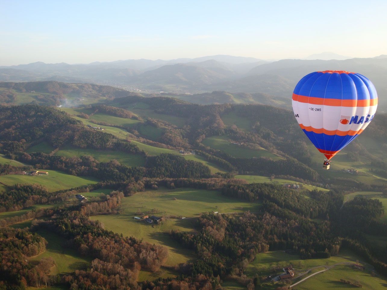 Teplovzdušný balón nad zelenou kopcovitou krajinou v Traisentalu.