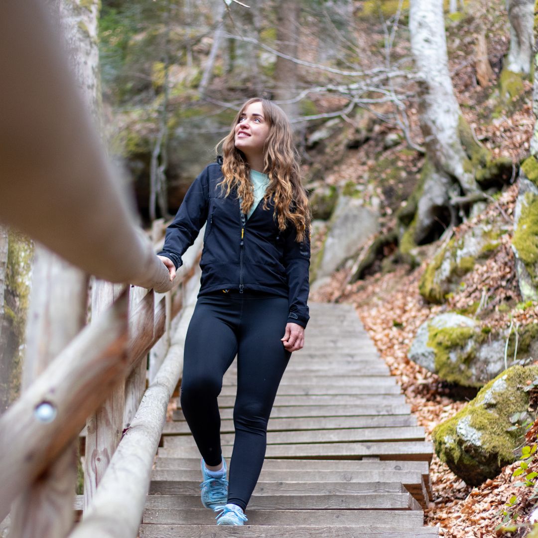 Žena kráča po drevených schodoch v zalesnenej oblasti.