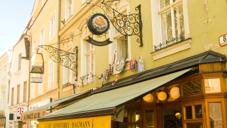 Exteri&eacute;rov&yacute; pohľad na Konditorei Hagmann so žltou strie&scaron;kou a pouličnou kaviarňou.