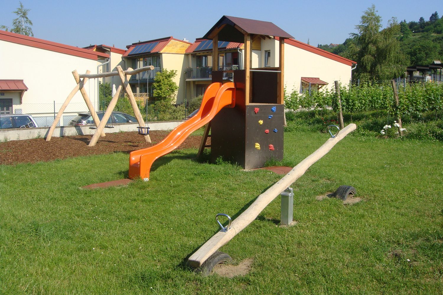 Detské ihrisko so šmýkačkou, hojdačkou a hojdačkou na lúke pred obytnými budovami.