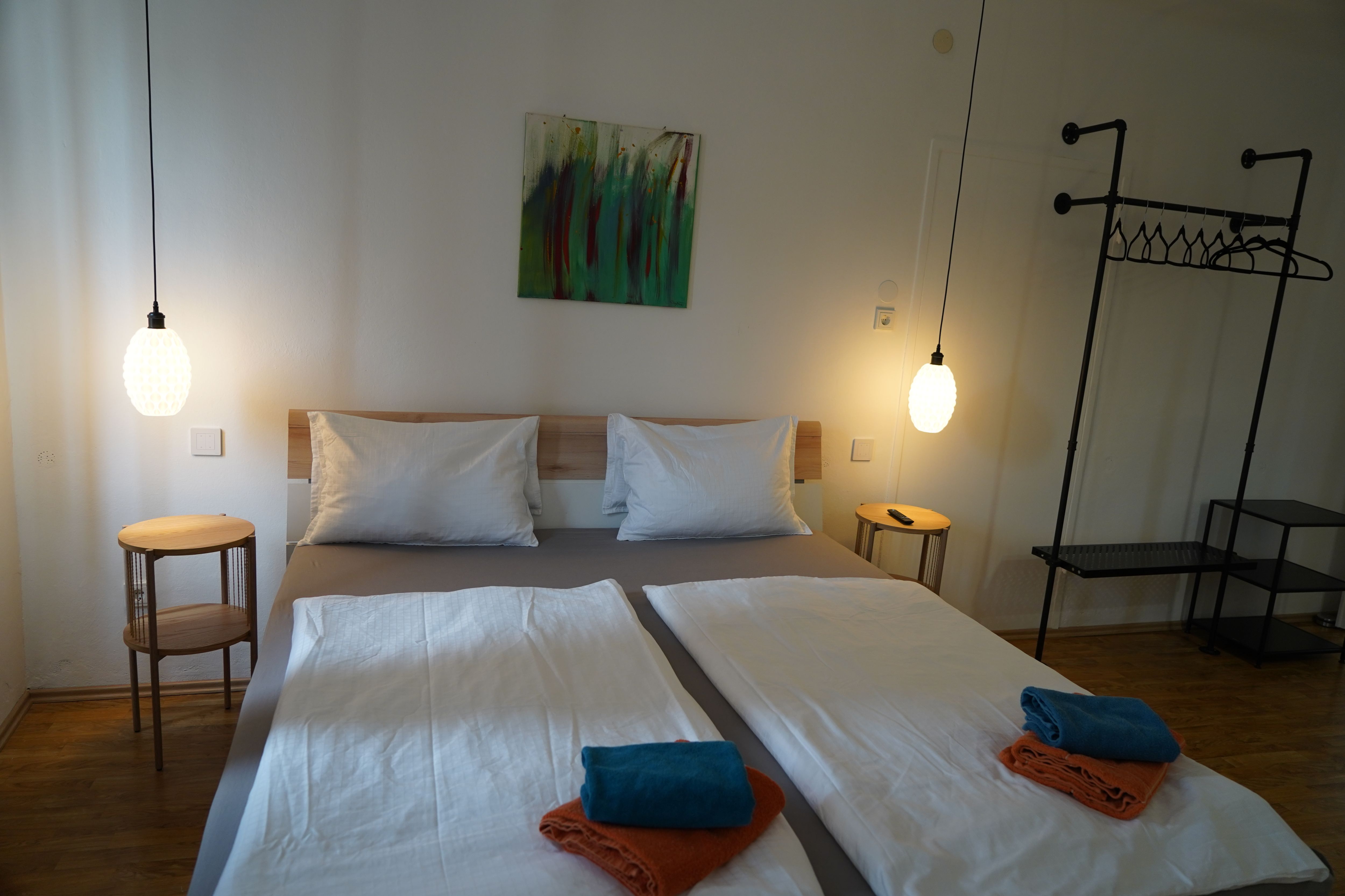 Moderná spálňa s manželskou posteľou, dvoma nočnými stolíkmi, závesnými lampami a uterákmi na posteli.