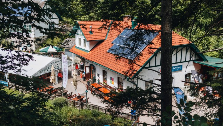 Tradičný hostinec so solárnymi panelmi na streche, obklopený stromami.