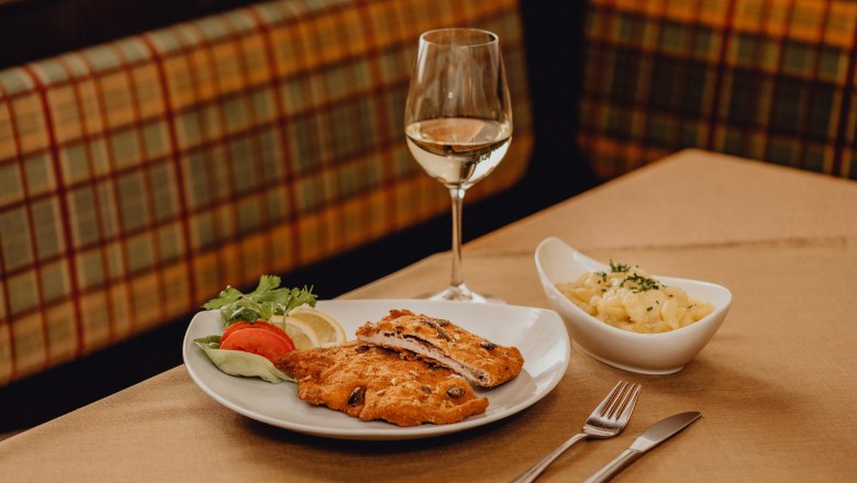 Na stole tanier cordon bleu, šalátová obloha a pohár bieleho vína.