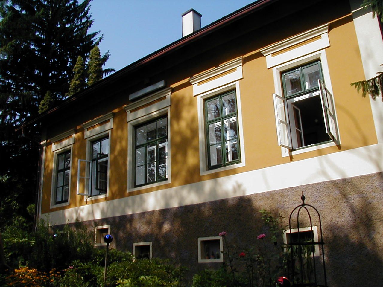 Žltý dom s otvorenými oknami a záhradou v popredí.
