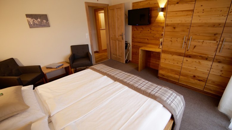 Spálňa s manželskou posteľou, dreveným nábytkom a TV na stene.