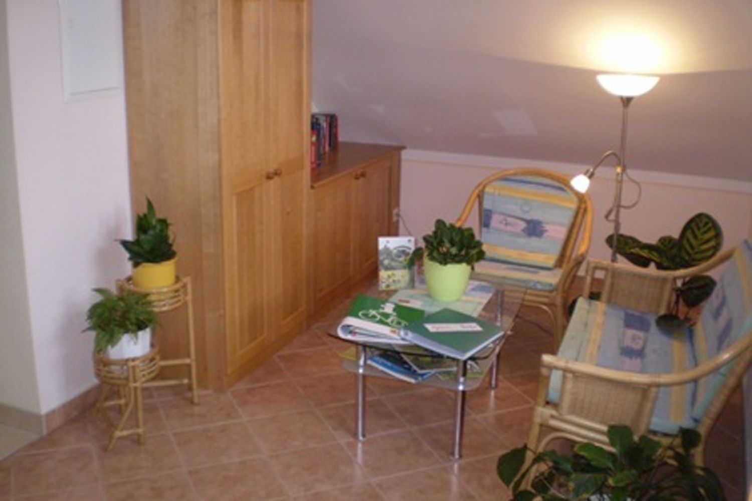 Útulný kútik na čítanie s ratanovým nábytkom, rastlinami a stolíkom s knihami.