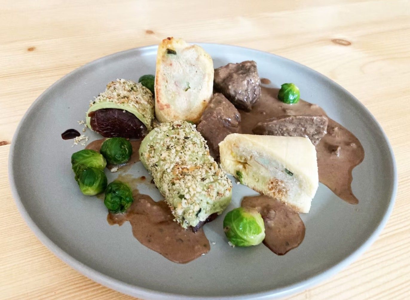 Na tanieri mäso, ružičkový kel a plnené pečivo na hnedej omáčke.