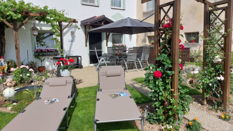 Z&aacute;hrada s ležadlami, pergolou a kvetinami.