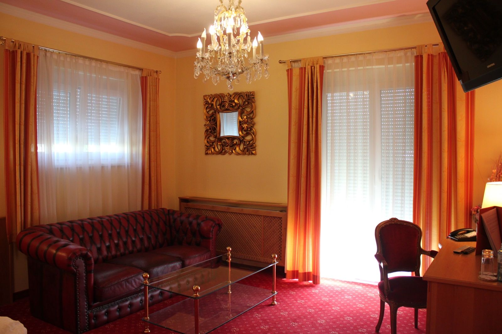 Elegantná obývacia izba s koženou pohovkou, skleneným stolom, lustrom a červenými závesmi.