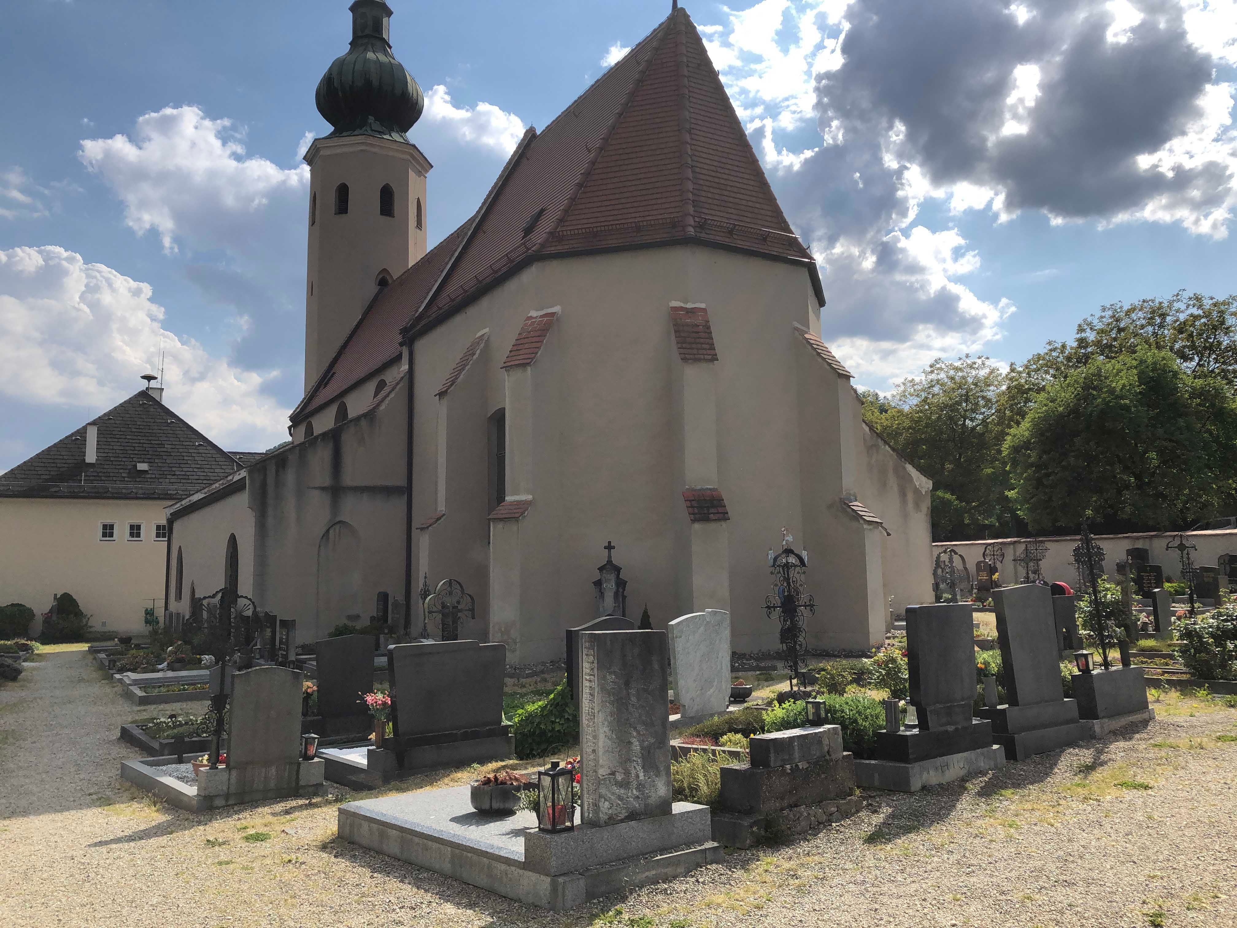 Kostol s cintorínom a náhrobkami v popredí, zamračená obloha.