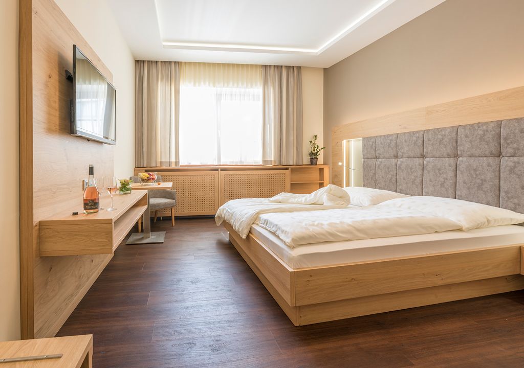 Moderná izba pre hostí s manželskou posteľou, TV s plochou obrazovkou a dreveným nábytkom.