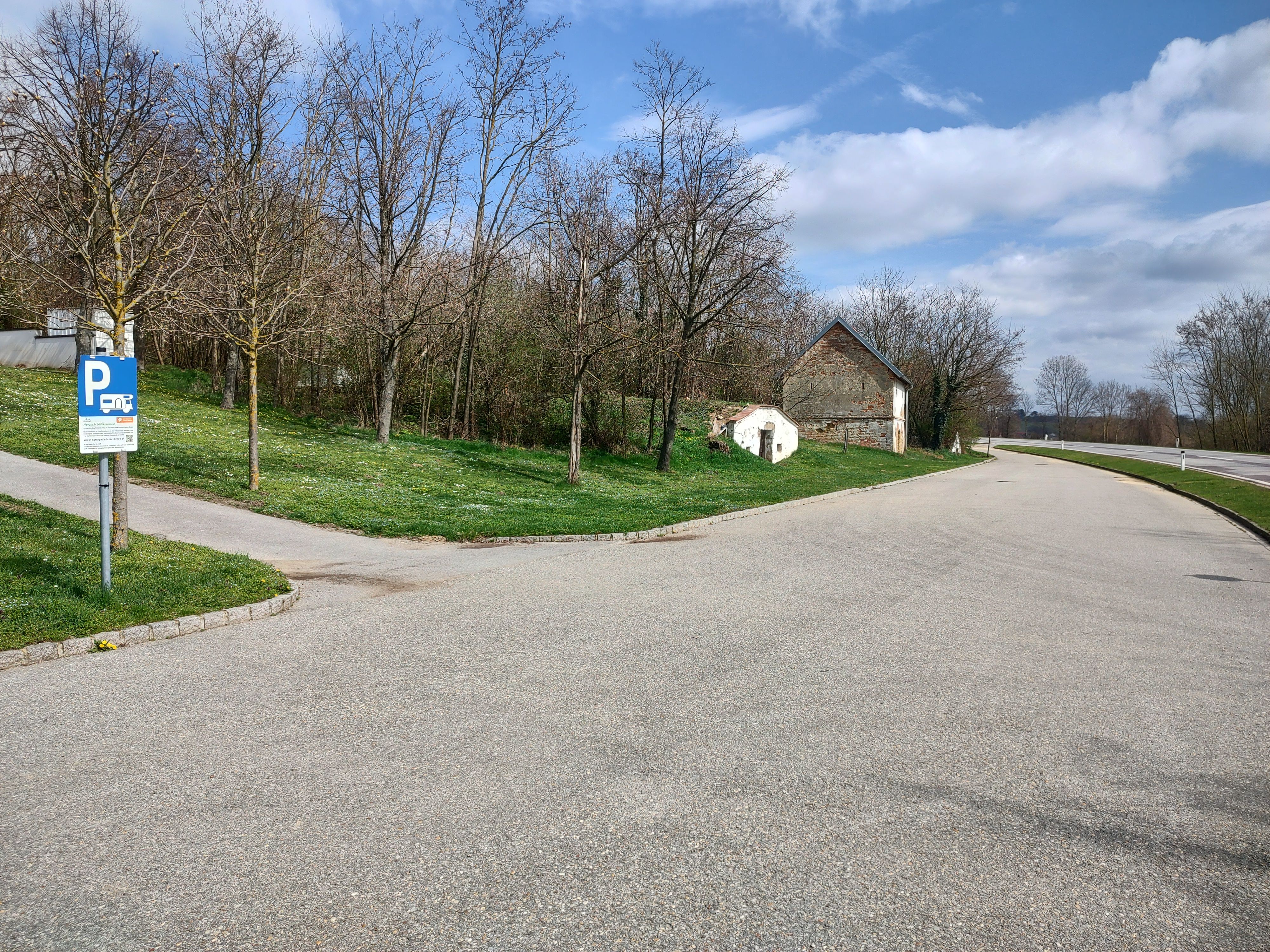 Parkovisko so značkou parkoviska pre obytné vozidlá, stromy a stará budova v pozadí.