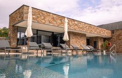 Exteriérový pohľad na moderný hotel s bazénom a ležadlami.