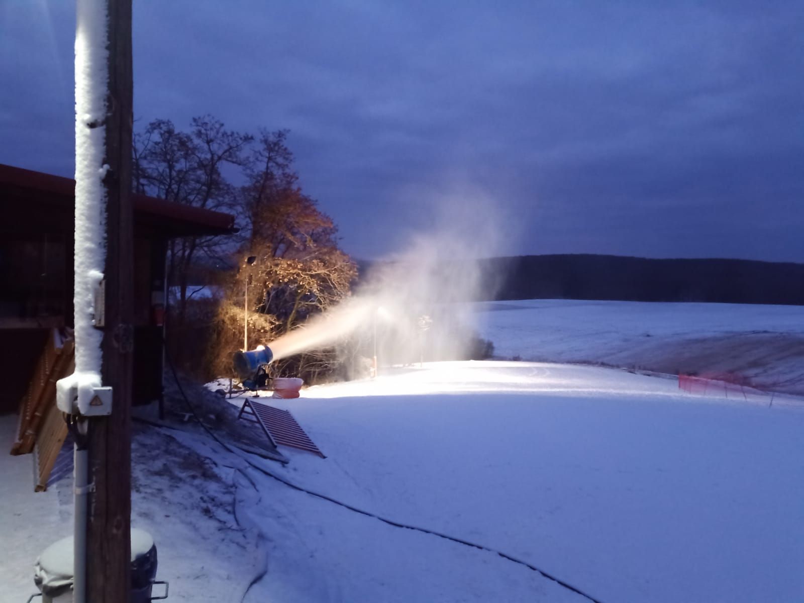 Snehové delo vyrába sneh na zjazdovke za súmraku.