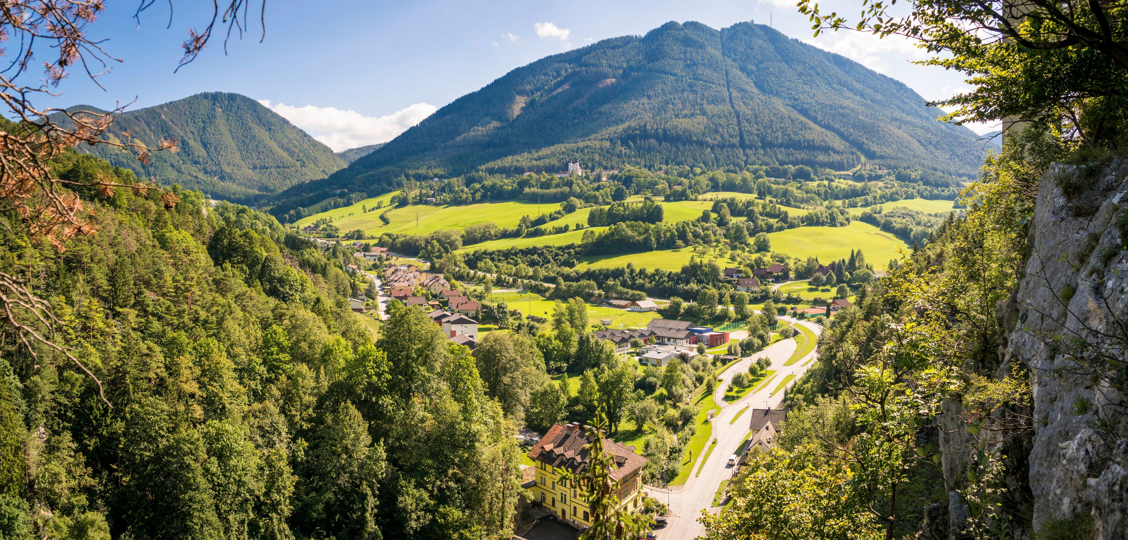Panoramatický pohľad na zelené údolie s horami v pozadí a dedinou v popredí.