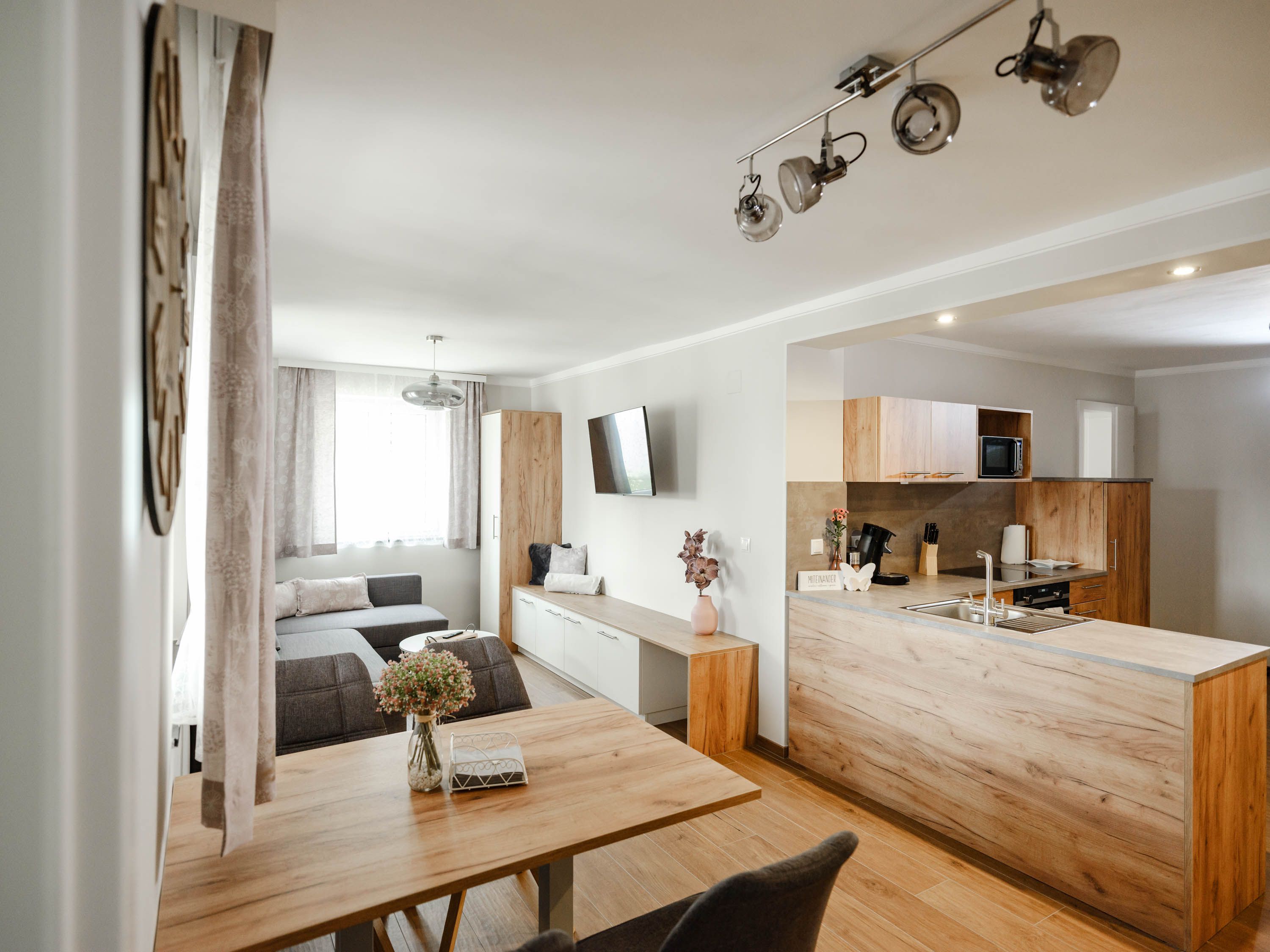 Moderná kuchyňa s dreveným nábytkom a sivou pohovkou.